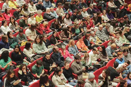 Dans une assemblée de fauteuils rouges, des dizaines de jeunes sont assis.
