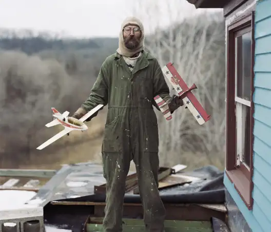 Alec Soth Homme debout dans la neige habillé chaudement qui tient une maquette d'avion dans chaque main