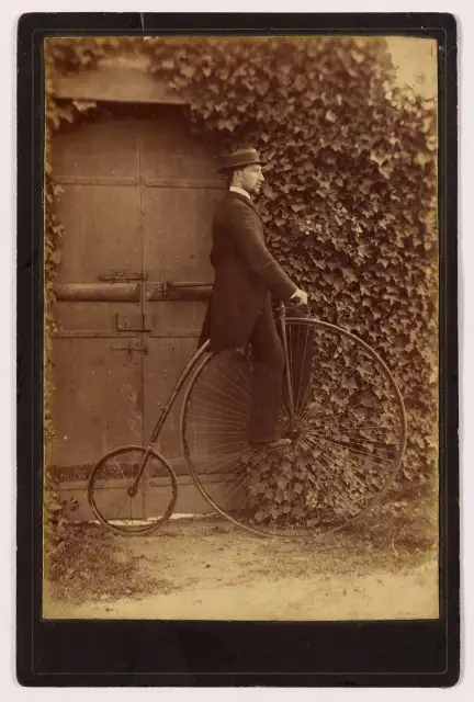 L’homme se tient à la porte pour ne pas tomber. Les roues de ces grand bi font parfois jusque 2,20m ! Il est donc bien impossible de rester sur la selle à l’arrêt.