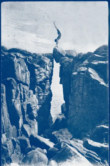 Et si, les falaises bretonnes étaient un terrain de jeu… La photographie représente une falaise de rochers qui occupe les deux-tiers de l'image en hauteur, avec le ciel pour le reste de l'image. Au centre, une faille nous permet de voir la mer. La faille est refermée en partie haute par un rocher sur lequel se tient une personne en équilibre sur les mains, de profil