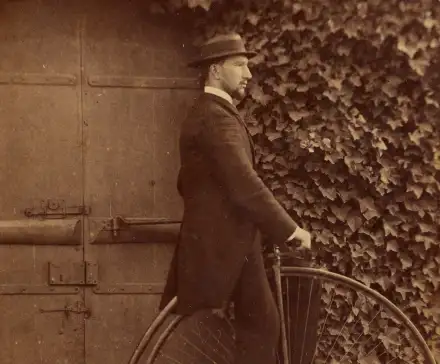 L'homme se tient à la porte pour ne pas tomber. Les roues de ces grand bi font parfois jusque 2,20m ! Il est donc bien impossible de rester sur la selle à l’arrêt