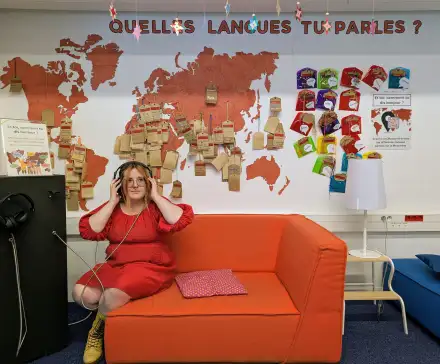 Photo de Louise assise sur un canapé, avec un casque d'écoute sur les oreilles